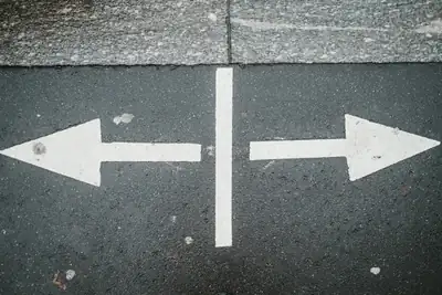 Two white arrows pointing in opposite directions on asphalt, representing a decision point